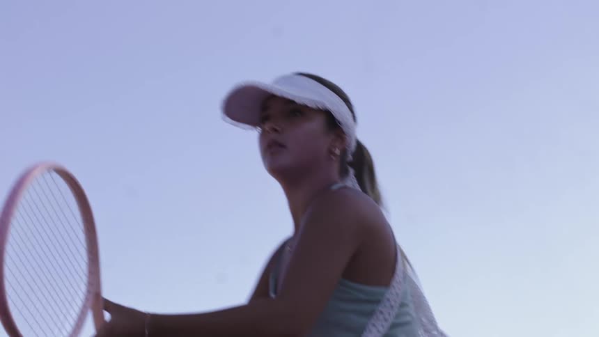 A woman wearing a cap is hitting a tennis ball using a pink racket