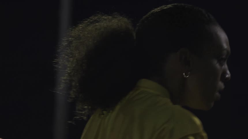A female athlete wearing a yellow jersey stands on the field at night taking a sip from a water bottle under the stadium lights