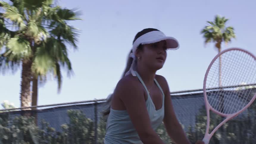 A young woman holds a tennis racket on an outdoor court appearing focused and ready
