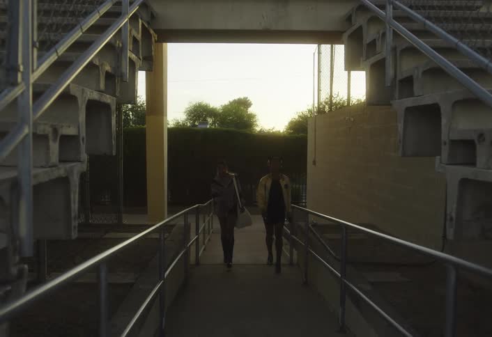 Two black females walks into a stadium with tracks and green grass at sunset