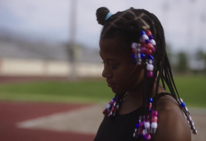 Young female black athlete stretches and exercises while sitting on a race track during daytime