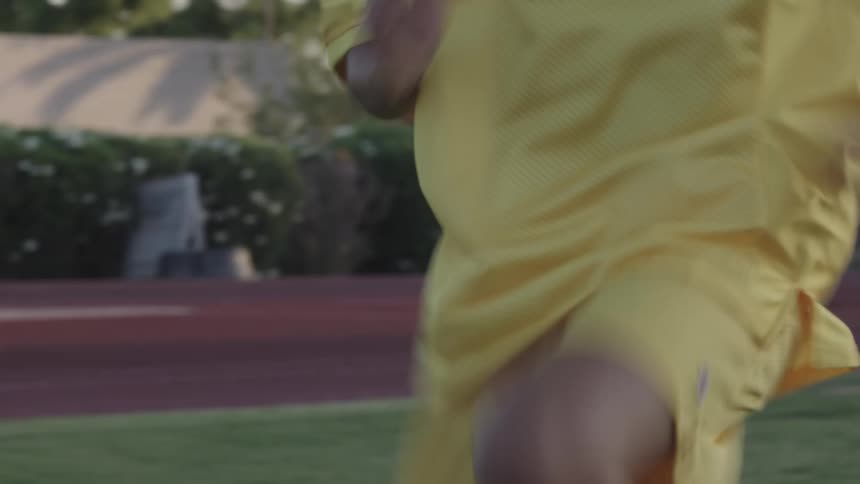 A woman in red cleats and wearing yellow uniform clothes is warming up by doing small jumps and running in place