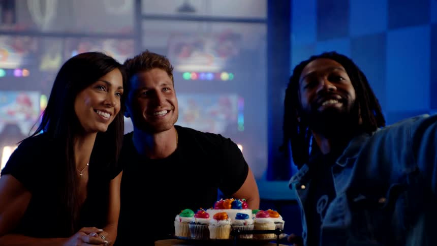 Three friends smile for a selfie with cupcakes in a colorful game arcade