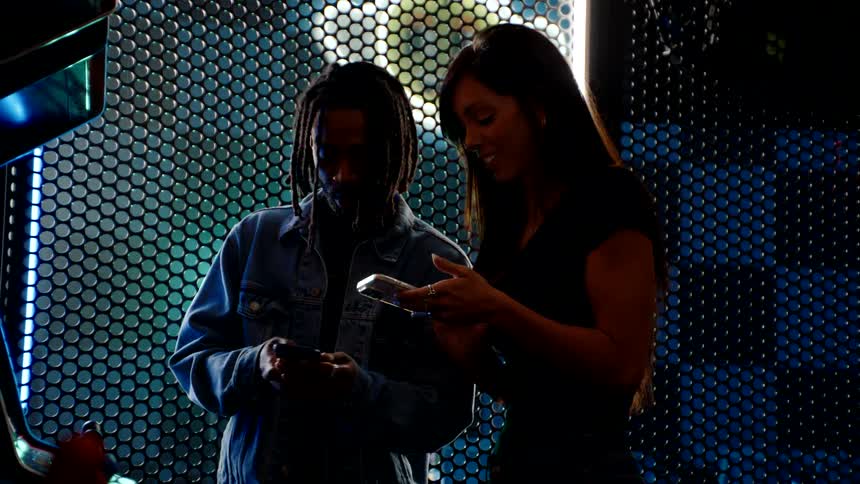 A black man talks with a young woman in an arcade store as they smile and exchange phone numbers
