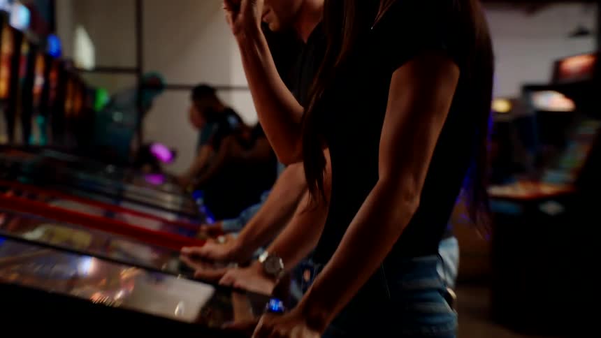 People are playing video games and pinball in the arcade