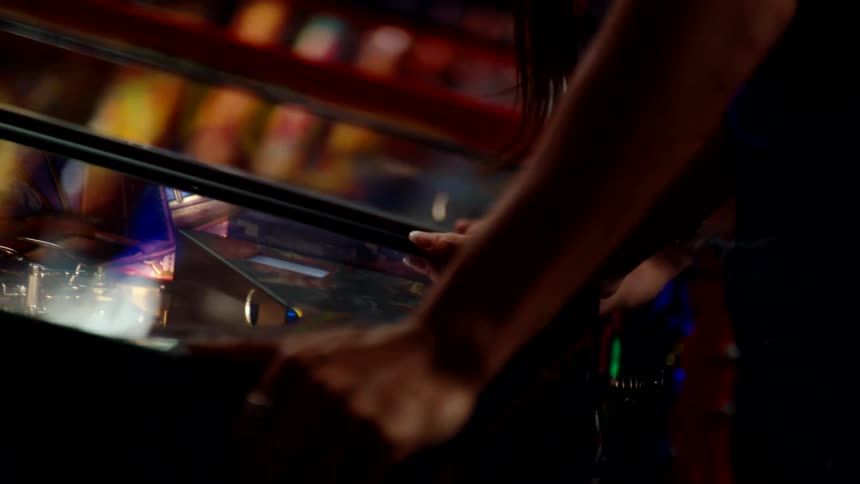 Close up of a woman playing arcades at a machine indoors with friends at night