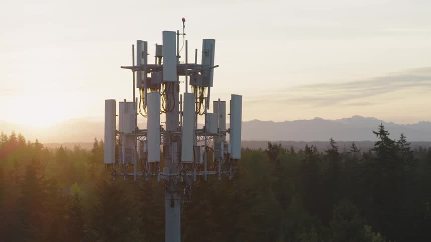 Morning sunshine filters through the panels of a 5G cell tower with mountains and a painted sky in the distance