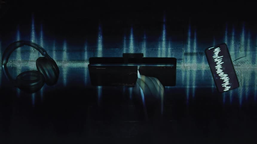 Light pattern plays over a person writing with a stylus on a surface sittingbetween a smartphone and a pair of headphones