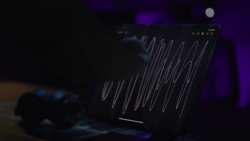 A persons hand using a white colored pen to make line drawings on a small black board