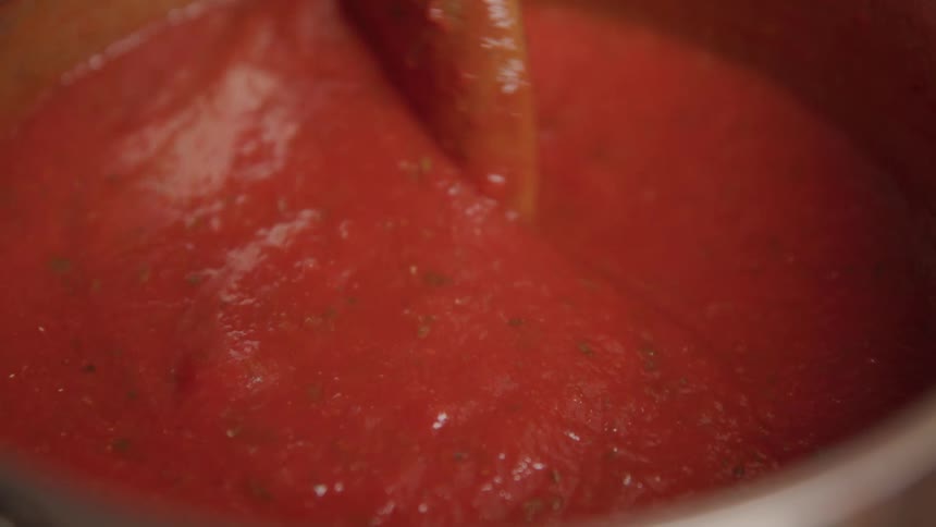 A wooden spoon stirs thick red tomato sauce in a pot