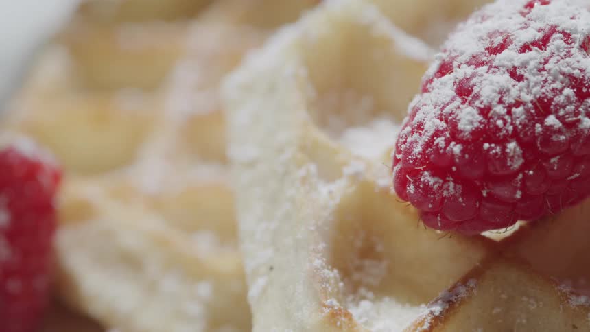 Powdered sugar sprinkles onto waffles topped with raspberries