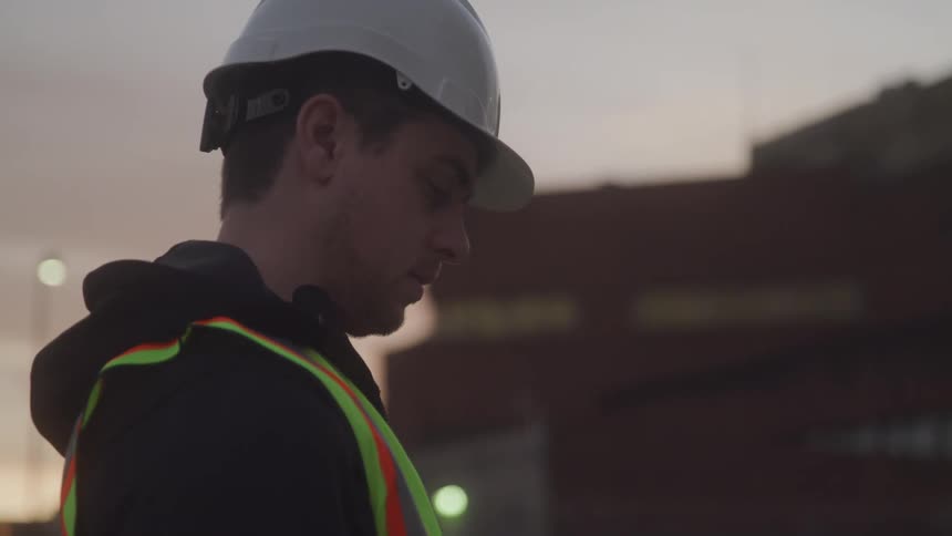 Construction worker is standing in the outskirts of the city at dusk