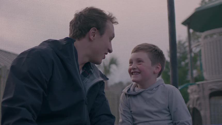 Father and son sit smiling at each other during a fun moment outdoors