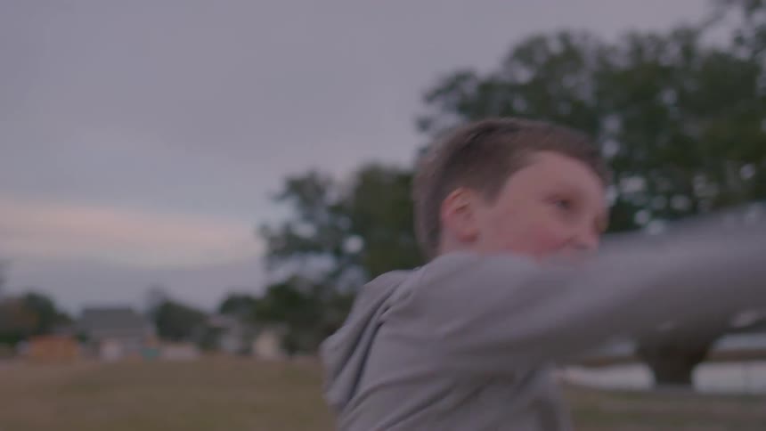 Close up of a boy throwing a baseball while standing outdoors at sunset