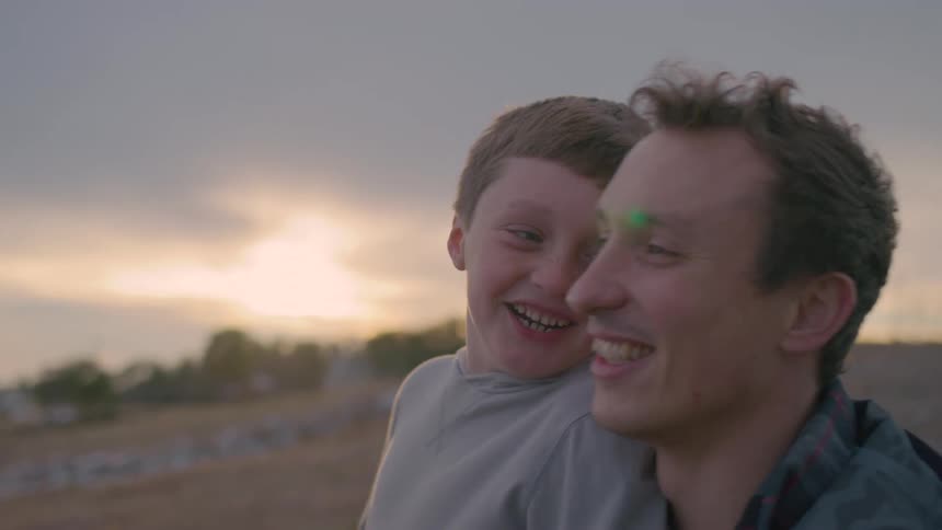 A smiling man and boy enjoy a happy moment outdoors at sunset