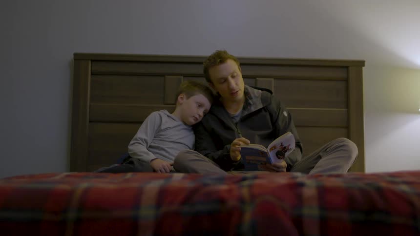 A father and son sit on the bed reading a bedtime story together