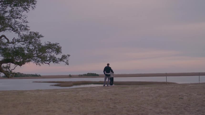Father and son stand by the water at sunset enjoying the peaceful nature view