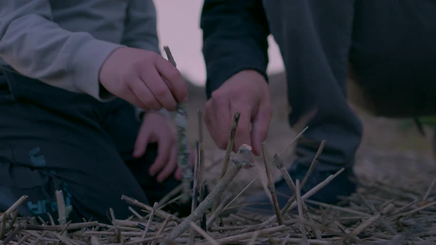 A man shows his son how to build a fire