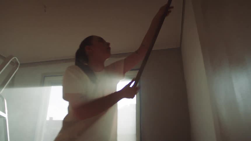 A woman is painting the walls in an empty room