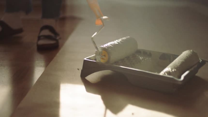 Close up of a paint roller rolled in a paint tray by a person standing in a room during daytime