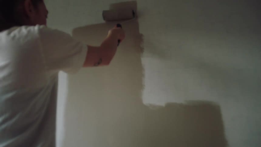 Woman paints a wall with a roller in a minimally furnished room