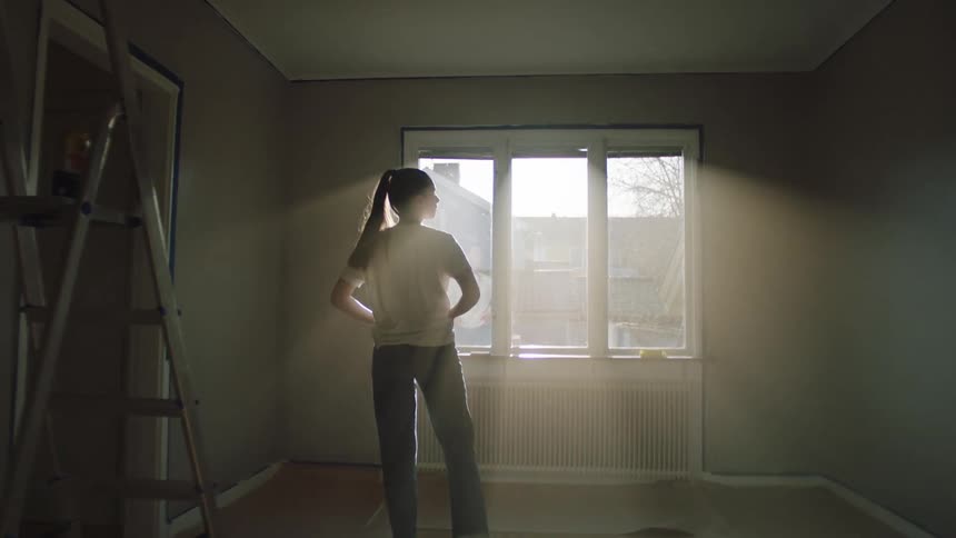 Female painter walks around a room inspecting painted walls during daytime