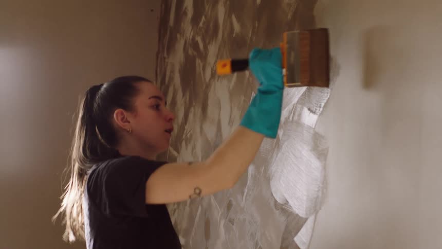 A woman paints a wall with textured strokes using a wide brush