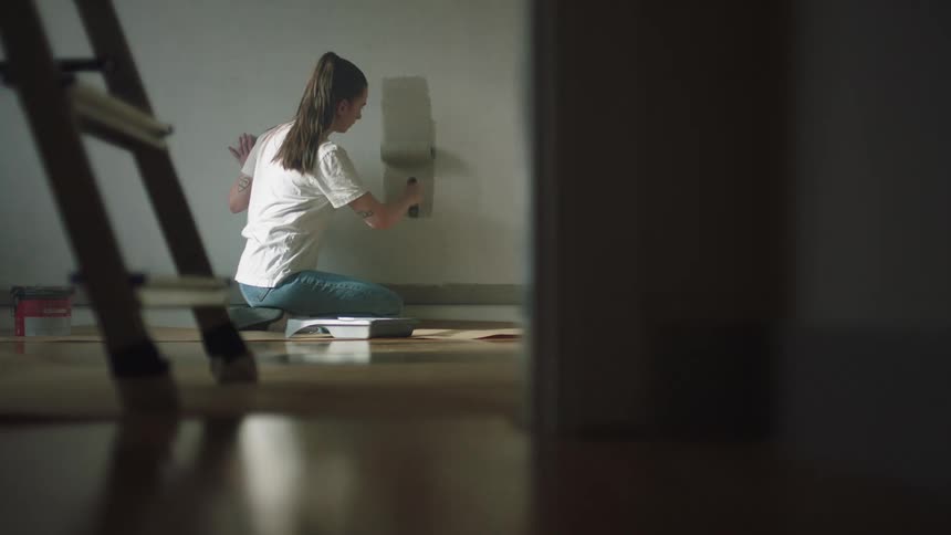 A woman is painting the wall with a roller
