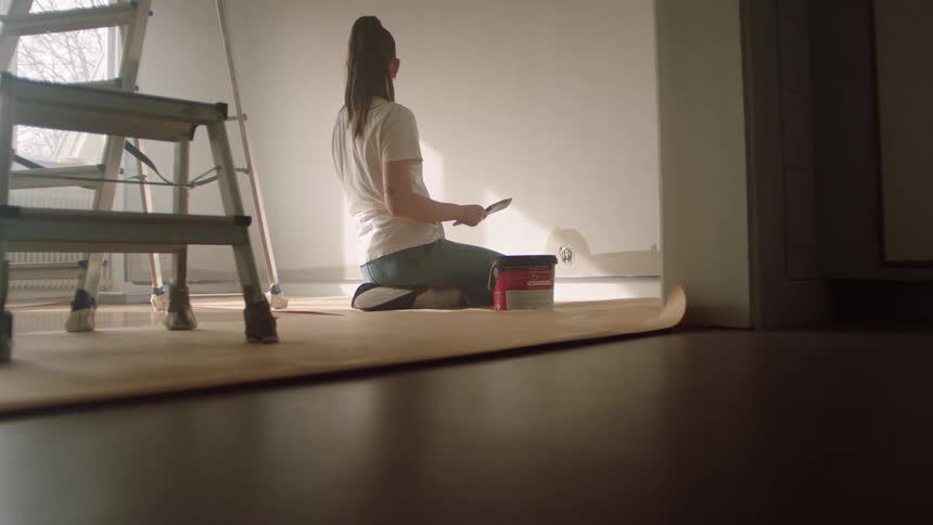 Woman sits on the ground as she paints the walls in her home