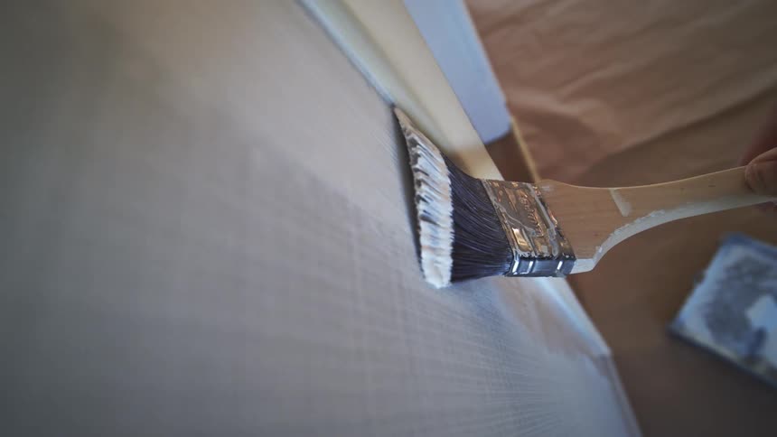 A brush is used to apply white paint to the wall at midday