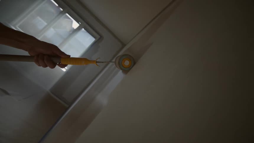 Persons arm holding a paint roller and painting a wall