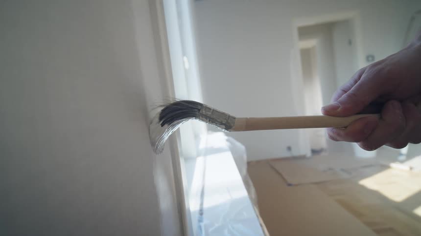 A persons hand using a paintbrush to paint a wall with white paint