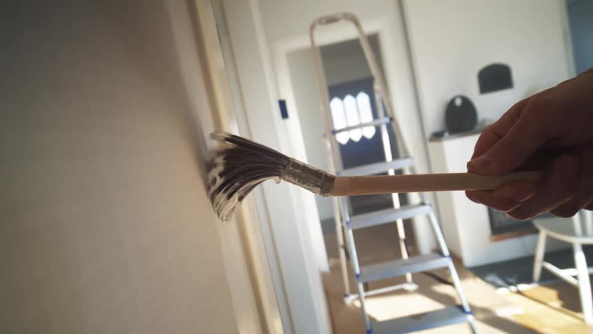 Close up of a painters hand holding a paintbrush while painting the interior walls of a room during daytime
