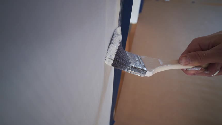 A persons hand holding a brush to paint a wall with white paint