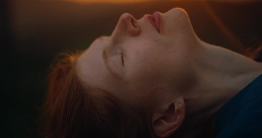 A woman lies on the ground outdoors as the orange setting sun casts its light on her