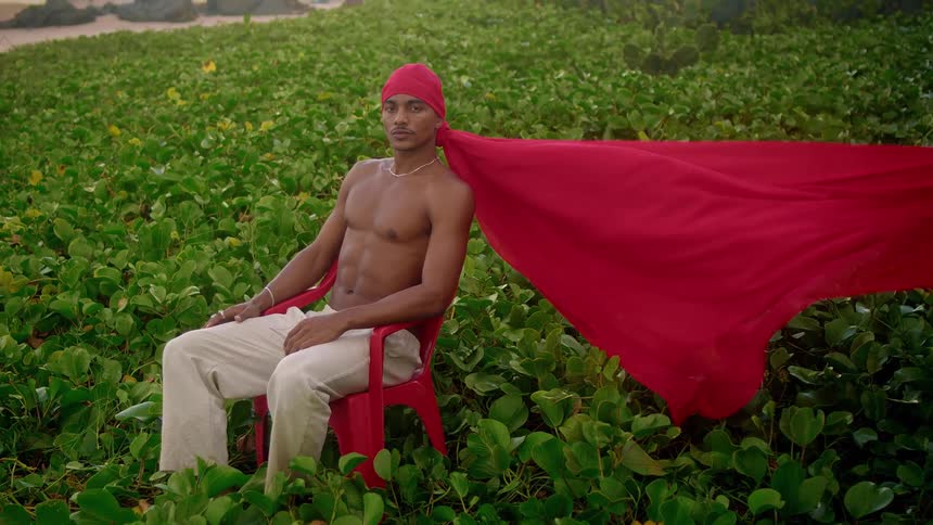 A man is wearing a long red do rag and sitting