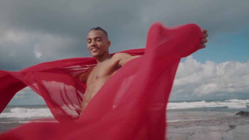 A man is draped with a red sheet on the beach