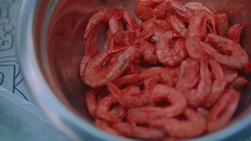 A metal bowl of shrimp sits on a blue and white tablecloth