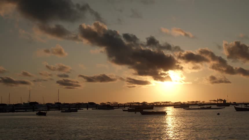 A beautiful cloudy sunset sky hangs over a marina where numerous boats are silhouetted on the calm water