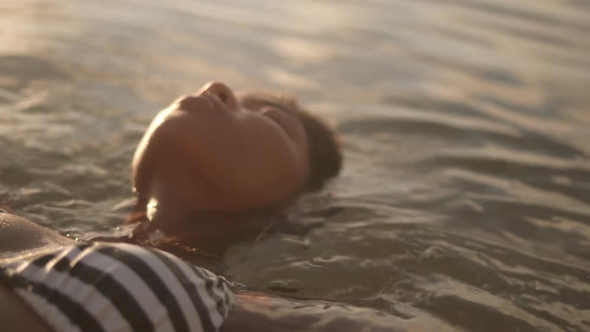 Woman is floating in ocean water with sun shining down