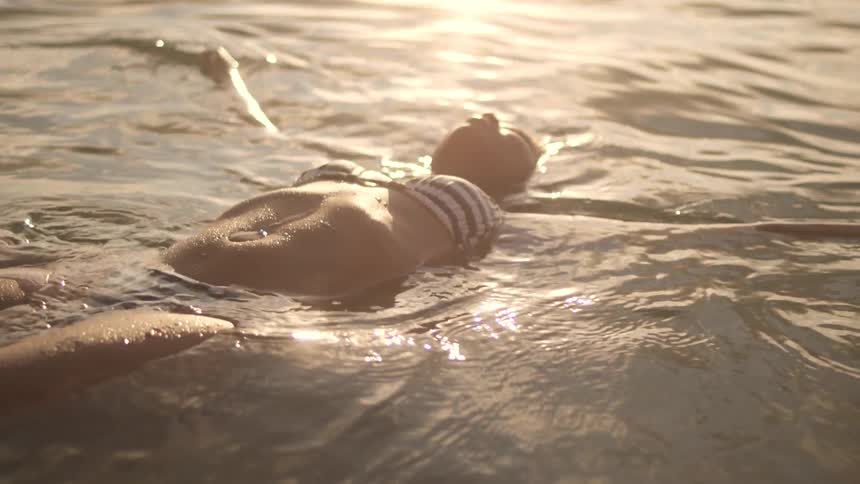 Woman in striped bikini floating on her back in a lake at sunset