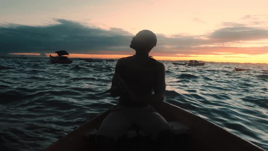 A man sits in a boat on the ocean at sunset gazing upward in peaceful contemplation