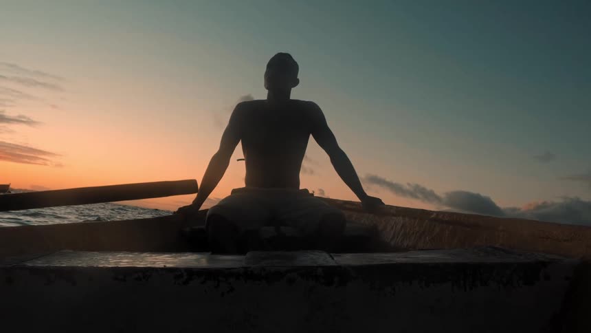 A man is sitting on the boat at sunrise