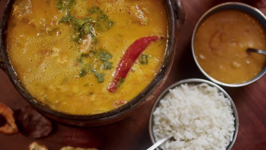 A big pot of yellow soup with vegetables and a bowl of rice on the table