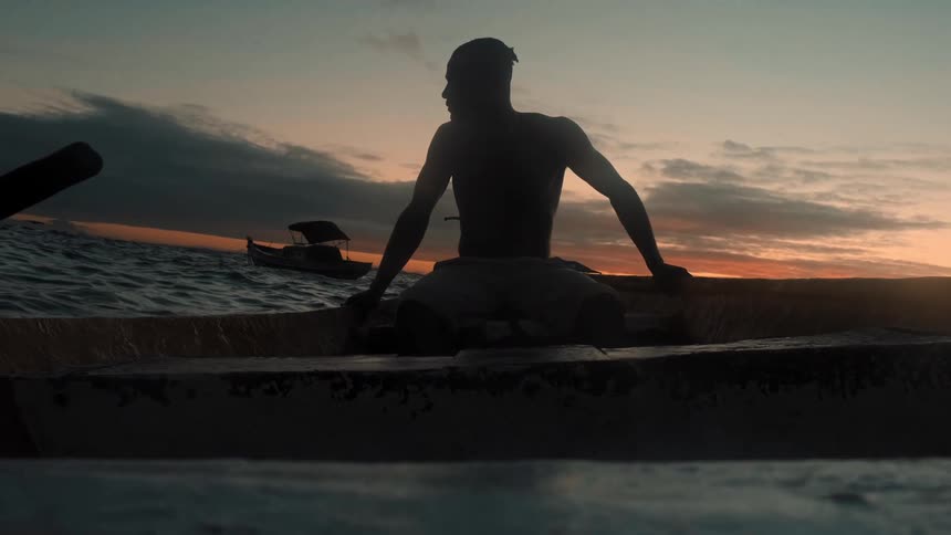 A man sitting inside a canoe at sunset