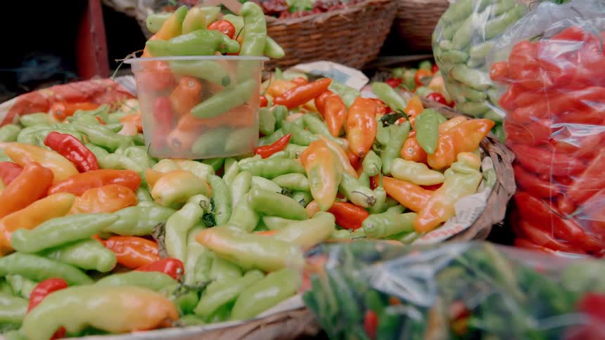 Display of green red and orange peppers displayed in baskets and clear bags