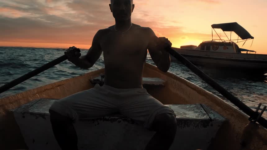 A man is rowing a boat at sunset