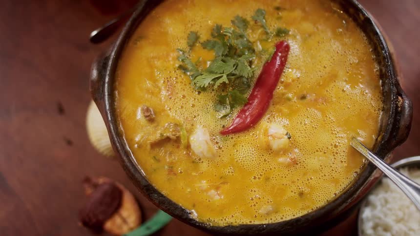 Steaming yellow curry garnished with cilantro and red chili on wood surface