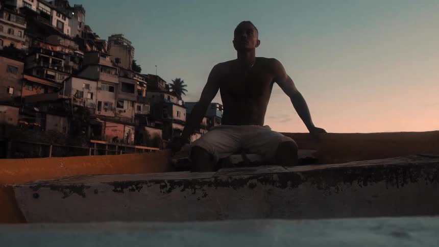 A person sits in a boat near the shore of a coastal town with sunset light hitting the homes climbing up the hillside