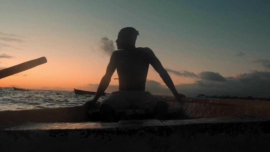 The man is looking towards the setting sun as he sits on the boat